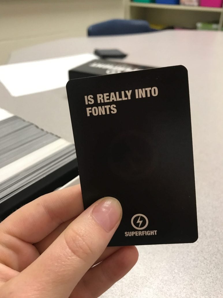 A hand holding a black SuperFight card that reads "is really into fonts."