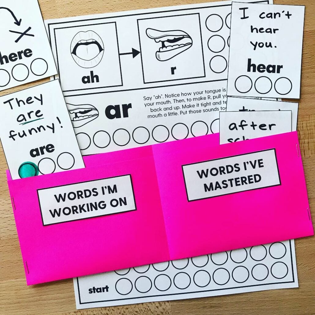 Speech practice worksheets and word cards arranged around two bright pink folders labeled “Words I’m Working On” and “Words I’ve Mastered.”